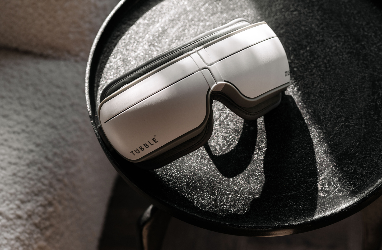 White Tubble eye massager resting on a textured black surface, lit by soft natural sunlight