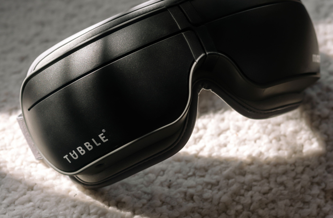 Close-up of a black Tubble eye massager resting on a soft, textured surface in natural sunlight