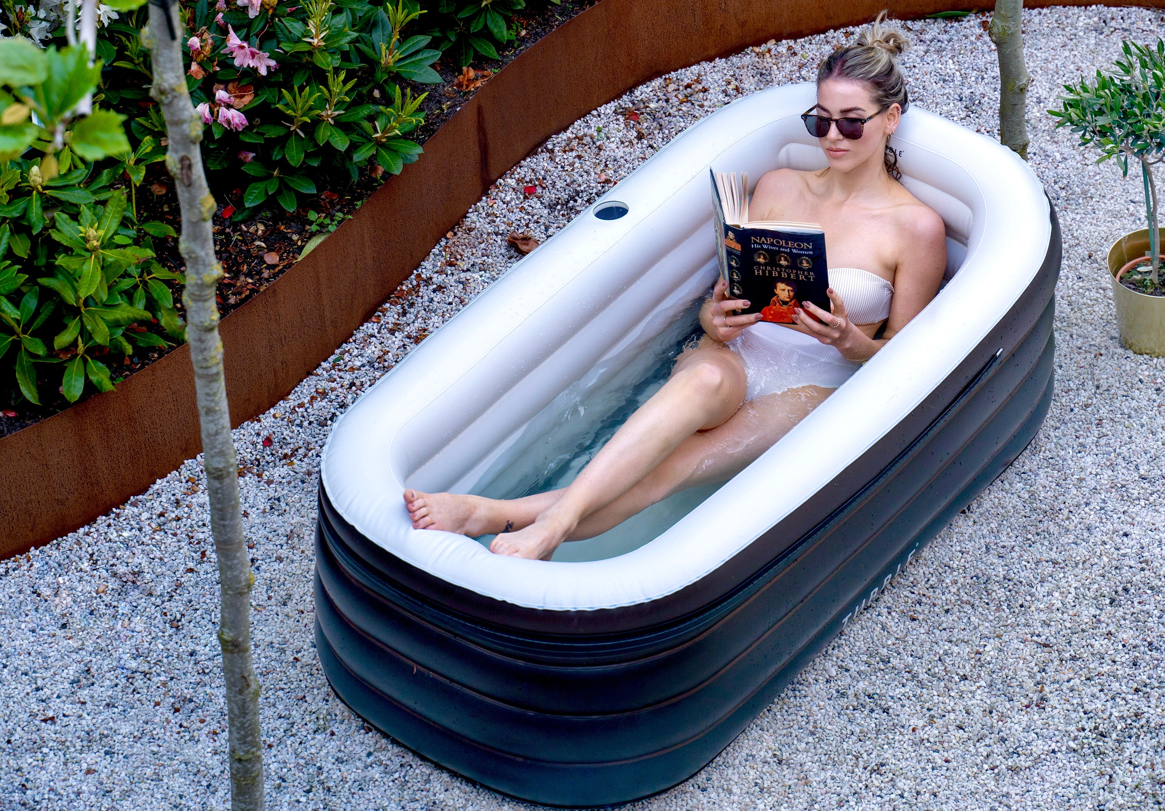 Woman reading a book in an inflatable bathtub outdoors.