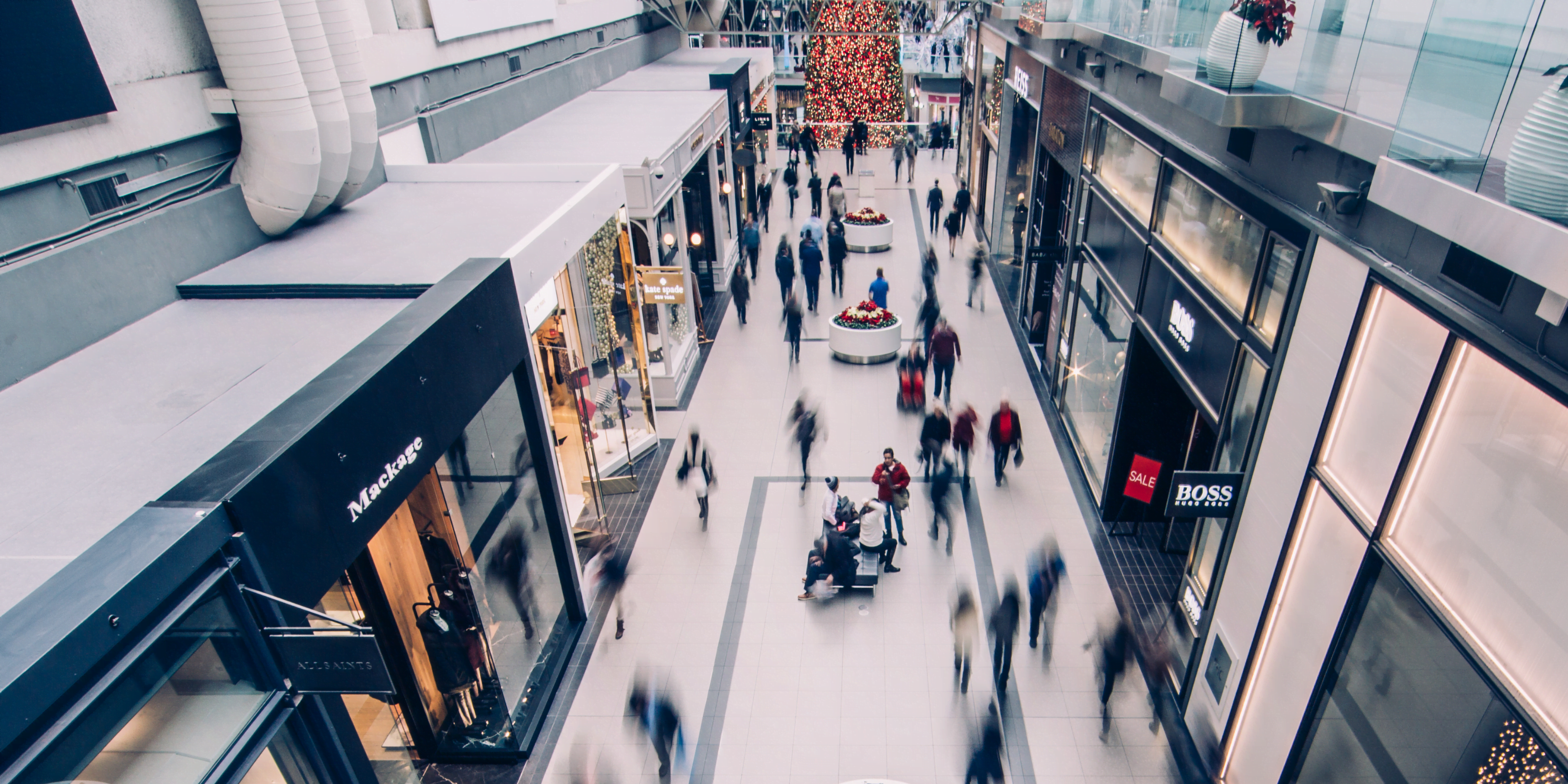 Crowded shopping mall with people walking between retail stores, used as lifestyle imagery for Tubble.