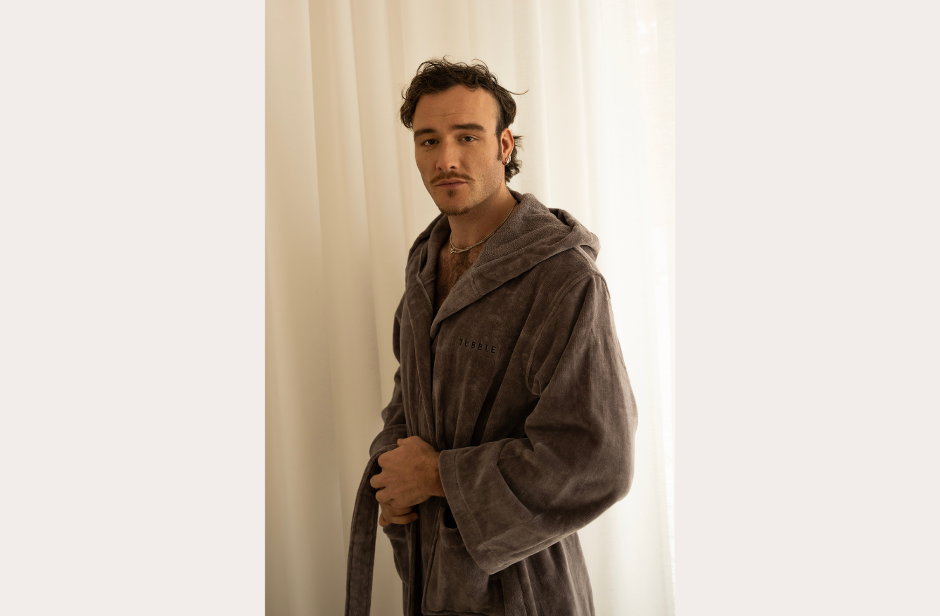 Man wearing a soft grey Tubble bathrobe standing in front of light curtains