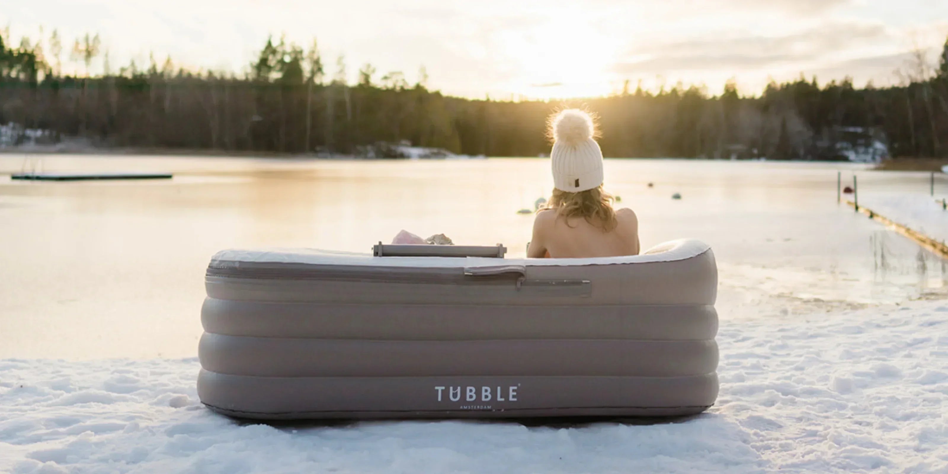 Person sitting in a Tubble inflatable bathtub outdoors on a frozen lake at sunset, enjoying a winter soak.
